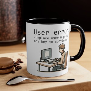May include: White ceramic mug with a black rim and handle. The mug features a black and white illustration of a person sitting at a computer with the text "User error: -replace user & press any key to continue."