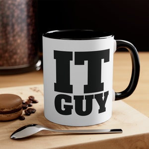 Könnte beinhalten: Weiße Keramiktasse mit schwarzem Rand und Henkel. Die Tasse hat den Text "IT GUY" in Schwarz aufgedruckt.