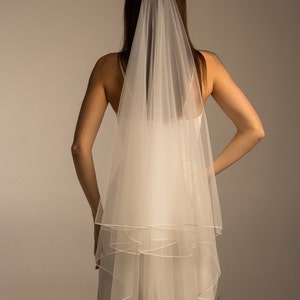 May include: A white single-tier bridal veil with a satin edge. The veil is made of soft tulle and is designed to be worn with a comb.