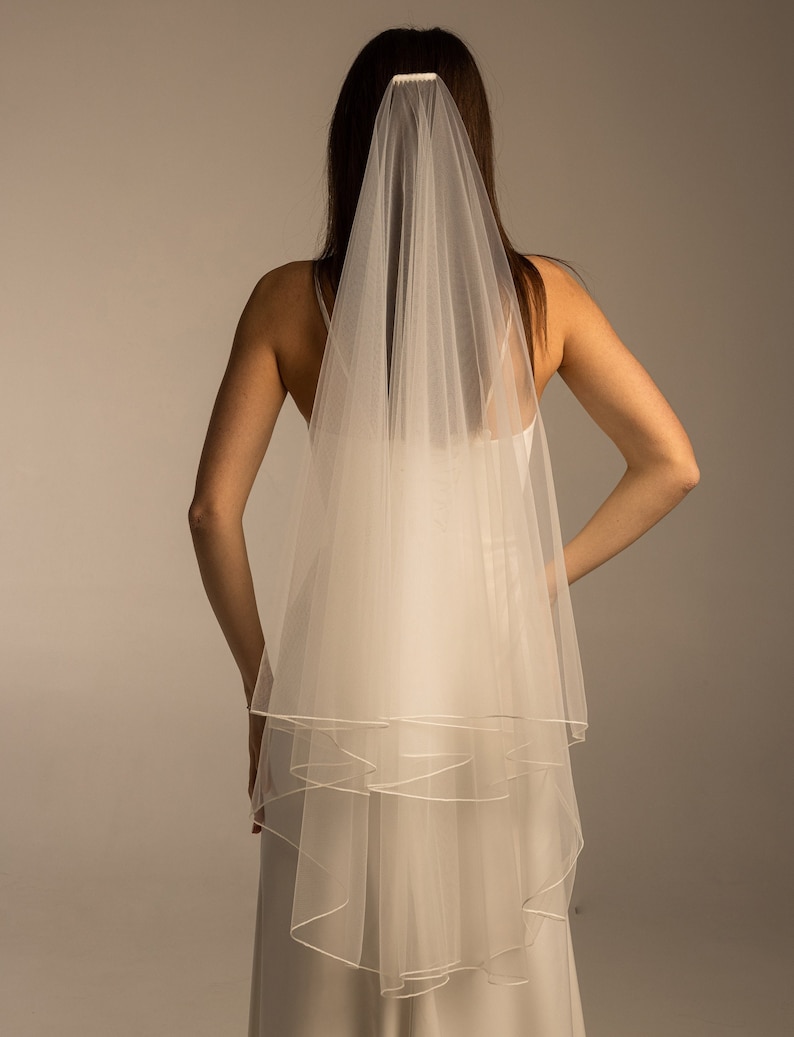 May include: A white single-tier bridal veil with a satin edge. The veil is made of soft tulle and is designed to be worn with a comb.