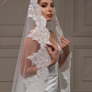 May include: A white wedding veil with detailed lace edging. The sheer veil drapes elegantly, with the text "LIKE VEIL" visible in the background. A bridal accessory.