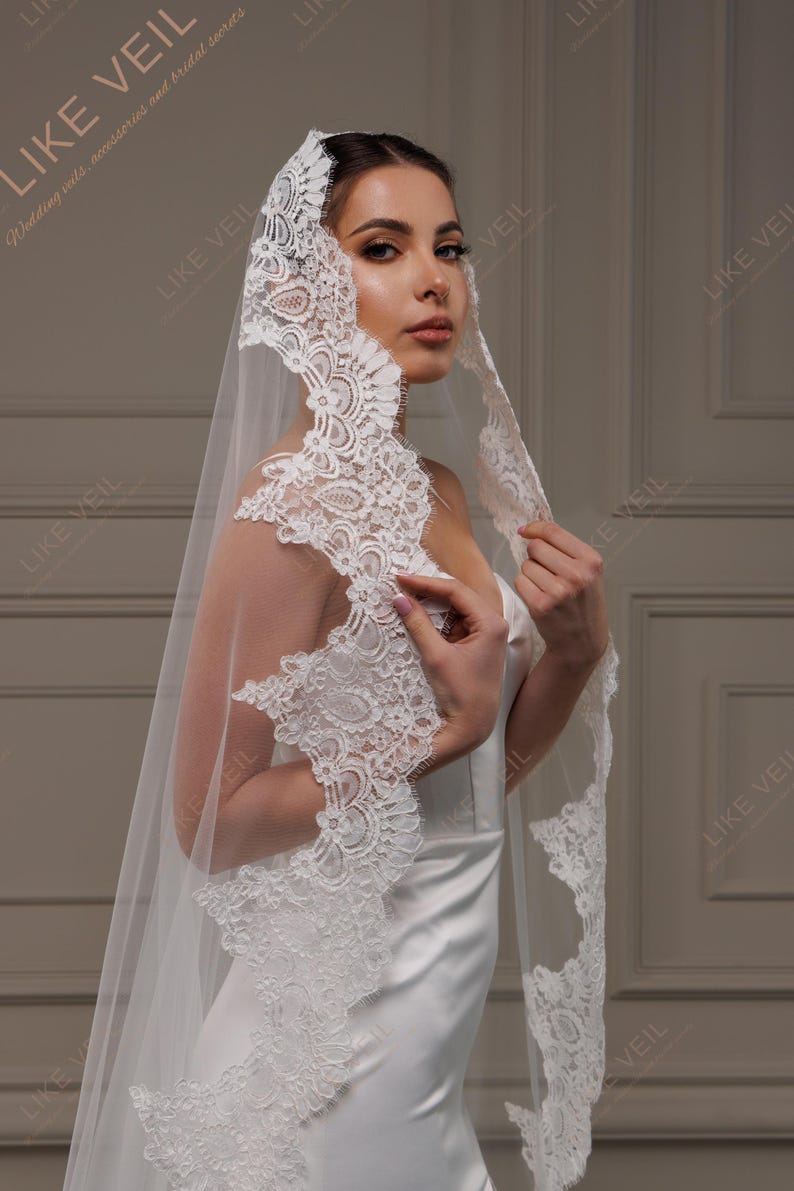 May include: A white wedding veil with detailed lace edging. The sheer veil drapes elegantly, with the text "LIKE VEIL" visible in the background. A bridal accessory.