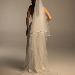 May include: A white bridal veil with a satin trim. The veil is long and flowing, with a single layer of tulle.