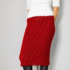 Könnte beinhalten: Ein knielanger, roter Strickrock mit diagonalem Rippenmuster und gerüschtem Saum. Der Rock wird mit einer gemusterten schwarzen Strumpfhose und dunkelroten Schnürstiefeln aus Leder kombiniert, dazu ein schlichtes weißes Langarmshirt.