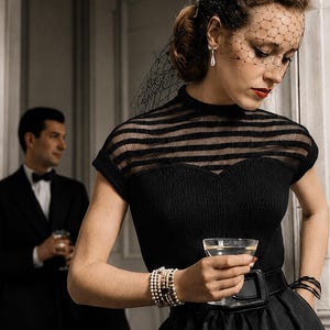 May include: A black short-sleeved top with a ribbed knit bodice and a sheer horizontal striped yoke, paired with a wide black belt and a black birdcage veil. The ensemble is accessorized with a multi-strand pearl bracelet and a teardrop earring.