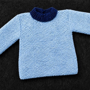 Könnte beinhalten: Ein langärmeliger Pullover mit einem hellblauen, strukturierten Strickkörper, einem dunkelblauen gerippten Kragen und passenden gerippten Bündchen an den Ärmelenden. Das Kleidungsstück hat einen klassischen Rundhalsausschnitt und einen geraden Saum.