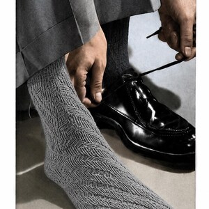 Könnte beinhalten: Ein Paar hellgraue Strickstrümpfe mit strukturiertem Fischgrätenmuster und geteilter Zehenpartie. Die Socken werden zu einer dunkelgrauen Hose und einem polierten schwarzen Lederschuh mit dünnen schwarzen Schnürsenkeln getragen.