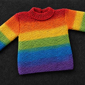 Könnte beinhalten: Ein langärmeliger Strickpullover mit einem lebendigen horizontalen Regenbogen-Farbverlauf. Das Kleidungsstück verfügt über einen gerippten Stehkragen und gerippte Bündchen und wechselt zwischen den Farben Rot, Orange, Gelb, Grün, Blau und Violett.