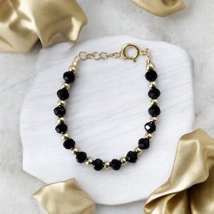 May include: A gold chain bracelet with black faceted beads. The bracelet has a lobster clasp closure.