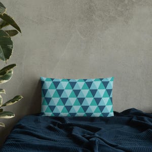 May include: A blue and teal geometric patterned throw pillow on a dark blue bedspread.
