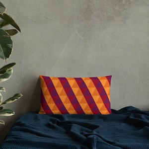 May include: A decorative throw pillow with a geometric pattern of orange and purple triangles. The pillow is on a dark blue bedspread.