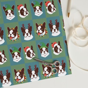 May include: A green and blue wrapping paper with a repeating pattern of Boston Terrier dogs wearing different festive hats and accessories. The dogs are wearing Santa hats, elf hats, reindeer antlers, and Christmas lights.