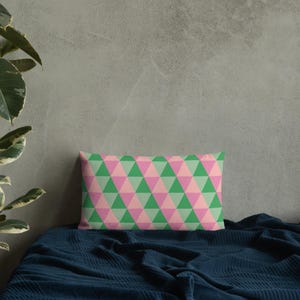 May include: A rectangular cushion with a geometric pattern of pink and green triangles. The cushion is on a blue bedspread.