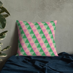 May include: A green and pink geometric cushion with a triangular pattern. The cushion is on a dark blue bedspread.