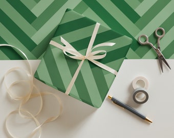 May include: A green and white striped gift box with a white ribbon and bow. The box is sitting on a white surface with a roll of tape, a spool of tape, and a pair of scissors.
