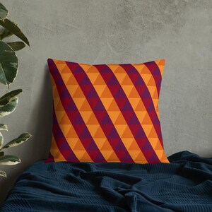 May include: A decorative throw pillow with a geometric pattern of orange and purple triangles. The pillow is on a dark blue blanket.