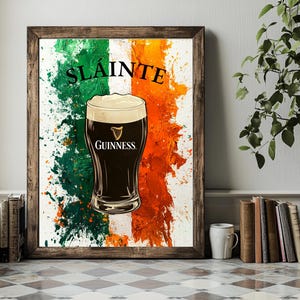 Puede incluir: Una impresión enmarcada con un diseño de bandera irlandesa estilizada que presenta un vaso de cerveza Guinness. El texto "Sláinte" está escrito en blanco sobre un fondo verde.