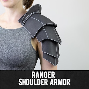 May include: A black shoulder armor piece featuring a layered, segmented design with visible white seam lines. The armor is constructed from multiple overlapping plates that curve over the shoulder. The text RANGER SHOULDER ARMOR is displayed in white capital letters at the bottom.
