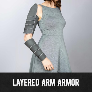May include: Gray layered arm armor with white trim. The armor is worn on the arm and shoulder. The text "LAYERED ARM ARMOR" is displayed in white on a black background.