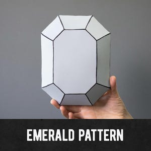 Könnte beinhalten: Ein weißes, geometrisches Objekt in Smaragdform mit schwarzen Umrissen wird vor einem grauen Hintergrund gehalten. Der Text "EMERALD PATTERN" wird in weißen, fetten Buchstaben auf einem schwarzen Banner am unteren Bildrand angezeigt.