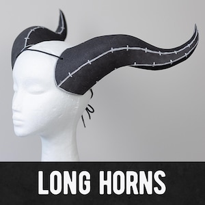 May include: A pair of long, black horns with white stitching. The horns are made of a flexible material and are designed to be worn as a costume accessory.