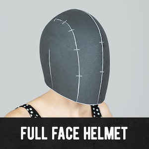 May include: A dark gray full-face helmet with white markings. The helmet is on a person wearing a black and white polka dot top. The text "FULL FACE HELMET" is at the bottom of the image.