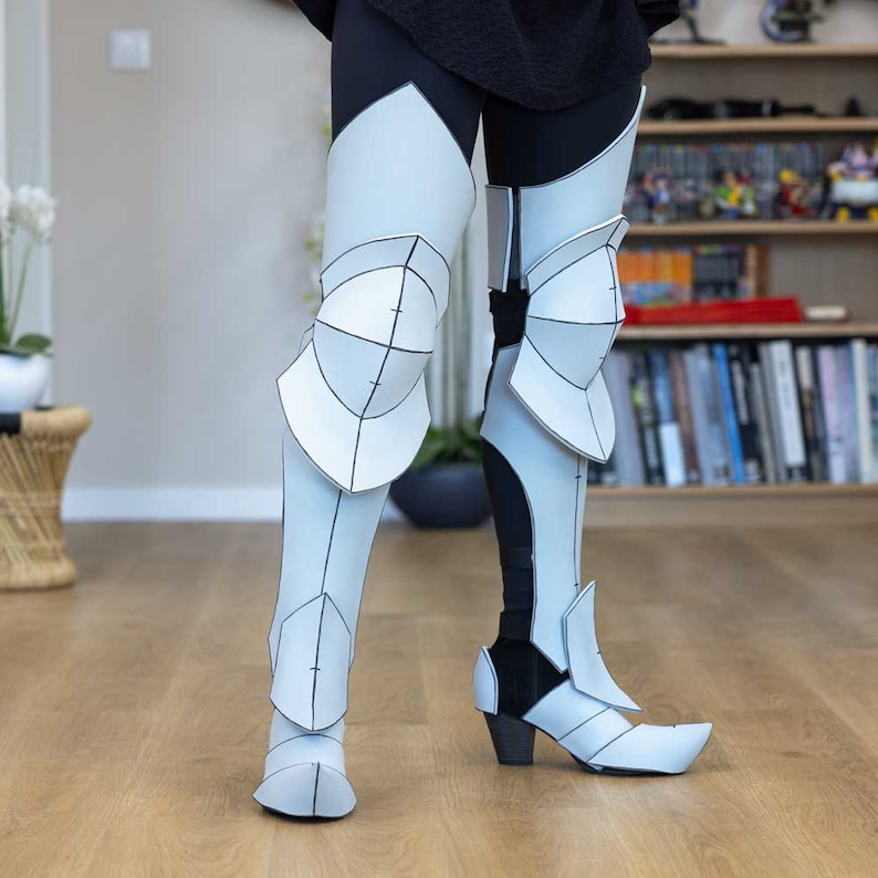 May include: White papercraft leg armor with black lines and details. The armor is worn over black leggings and includes knee pads and boots.