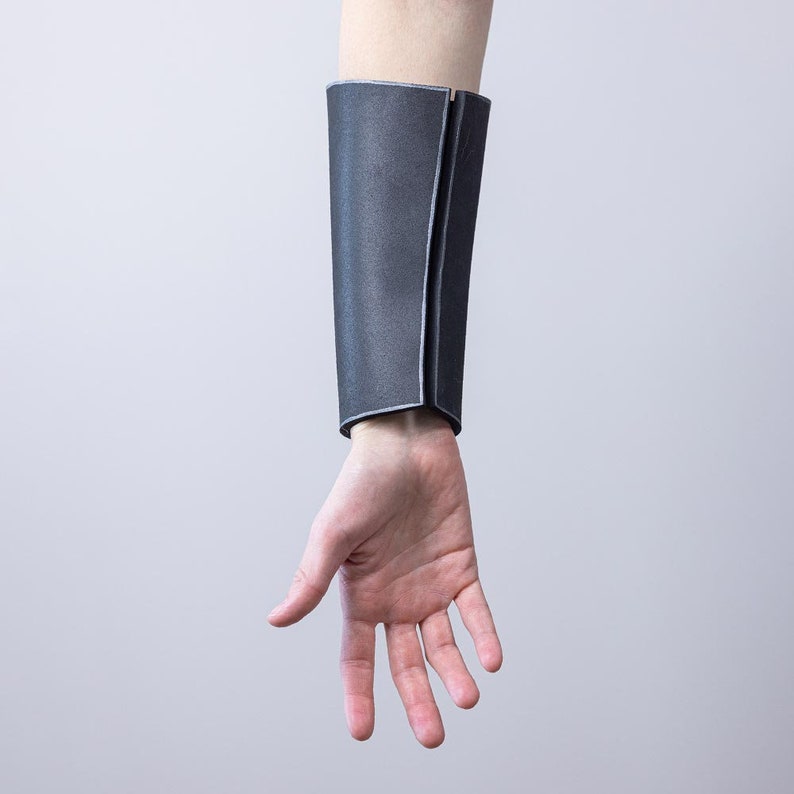 May include: A grey fabric arm cuff with a seam down the centre. The cuff is worn on the left arm.