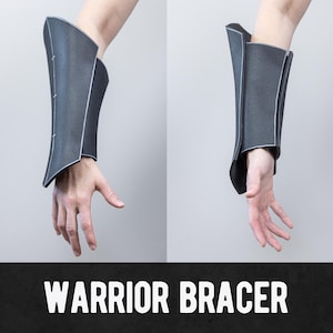 Könnte beinhalten: Zwei dunkelgraue Krieger-Armschienen mit weißer Umrandung werden gezeigt. Die Armschienen werden an den Armen einer Person vor einem hellgrauen Hintergrund gezeigt. Der Text "WARRIOR BRACER" befindet sich am unteren Rand des Bildes.