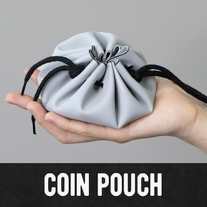May include: A light gray coin pouch with black drawstring closure. The pouch is held in a hand. The text "COIN POUCH" is displayed in white, bold letters on a black background.