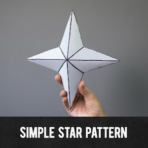 Könnte beinhalten: Ein weißer Papierstern mit schwarzen Umrissen wird vor einem grauen Hintergrund gehalten. Der Stern hat vier Spitzen und ein zentrales Design. Der Text "SIMPLE STAR PATTERN" wird in weißen Buchstaben auf einem schwarzen Banner am unteren Bildrand angezeigt.