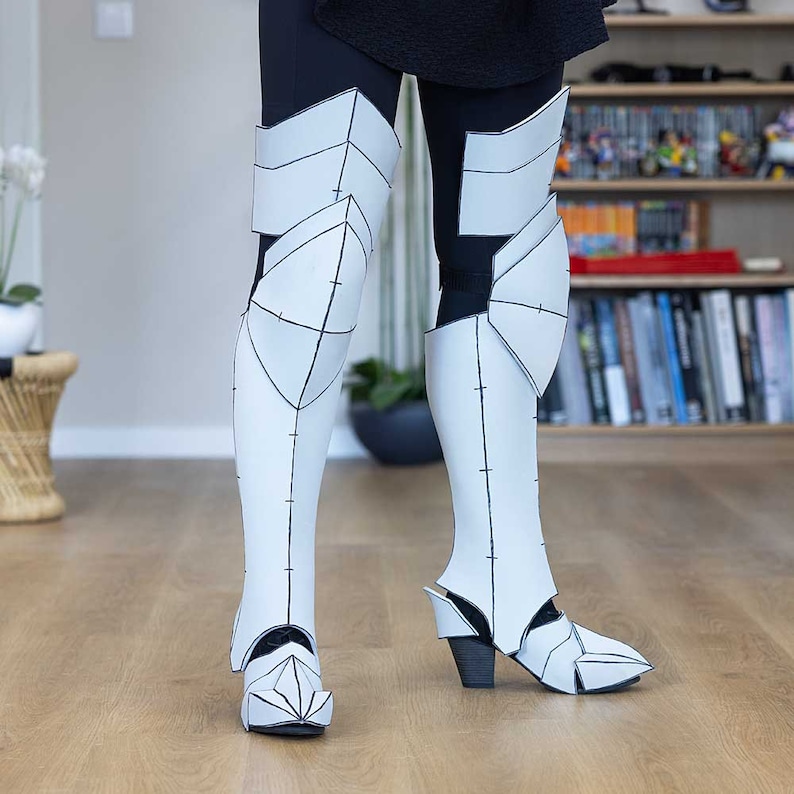 May include: White foam leg armor with black lines and markings. The armor is worn on both legs and extends from the knee to the ankle.