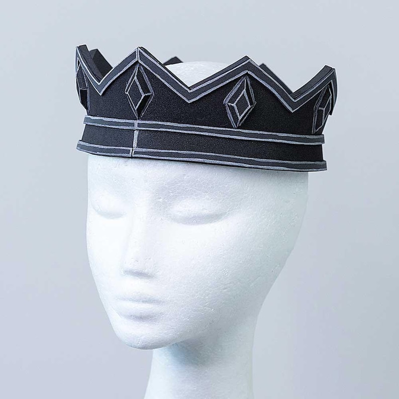 Op de afbeelding: Een zwarte schuimkroon met een diamantpatroon en zilveren accenten. De kroon wordt gedragen op een wit mannequinhoofd.