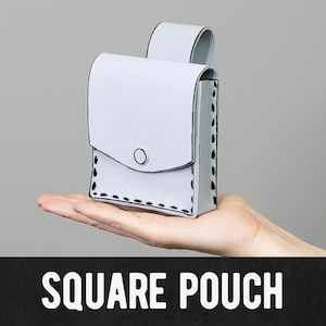 May include: A light gray square pouch with a flap closure and a button. The pouch has black stitching details and a loop on the back. The text "SQUARE POUCH" is displayed in white letters on a black background.