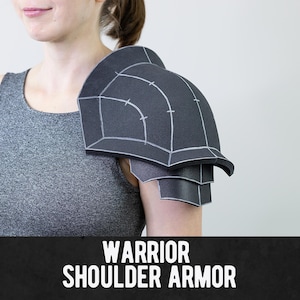 May include: A black foam shoulder armor piece featuring white drawn construction lines and a layered design. The armor is worn on one shoulder and is labeled with the white text WARRIOR SHOULDER ARMOR at the bottom of the image.