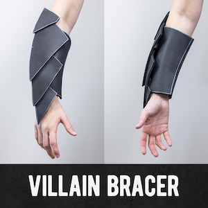 May include: Two views of a black Villain Bracer. The bracer is made of layered, angular shapes with white trim. The text "VILLAIN BRACER" is displayed in white letters on a black background.