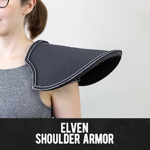 Op de afbeelding: Een zwart schouderharnas met een gebogen, puntig ontwerp en witte biezen langs de randen. Het harnas wordt op de schouder gedragen en bevat de tekst ELVEN SHOULDER ARMOR in witte hoofdletters onderaan de afbeelding.