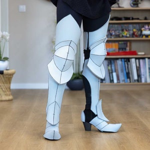 May include: White papercraft leg armor with black lines and details. The armor is worn over black leggings and includes knee pads and boots.