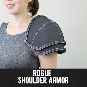 Può includere: Un pezzo di armatura per spalla in schiuma grigio scuro caratterizzato da un design curvo a strati con linee di costruzione bianche visibili lungo i bordi. L'armatura è etichettata con il testo ROGUE SHOULDER ARMOR in lettere maiuscole bianche.