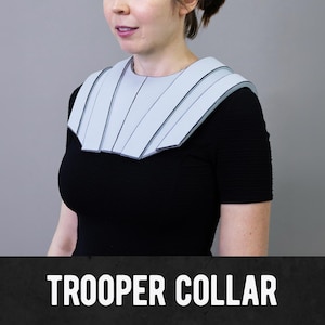 May include: A light blue Trooper Collar with black trim is worn over a black top. The collar has a layered design and is made of a rigid material. The text "TROOPER COLLAR" is displayed at the bottom of the image.