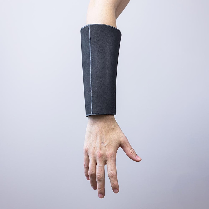 May include: A black fabric arm guard with a seam down the centre. The guard is worn on the forearm.