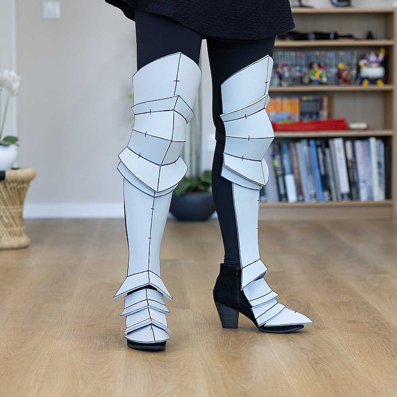 May include: White papercraft knee-high boots with a segmented design. The boots are worn over black leggings.