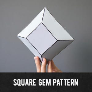 Puede incluir: Una gema cuadrada geométrica de papel blanco con detalles de contorno negro, sostenida sobre un fondo gris. El texto "SQUARE GEM PATTERN" se muestra en blanco sobre una pancarta negra.