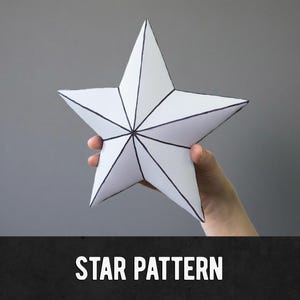 May include: A white, five-pointed star with black outline details is held against a gray background. The star is made of folded paper. The text "STAR PATTERN" is displayed in white, bold letters on a black bar at the bottom of the image.