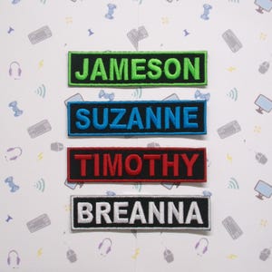 May include: Four embroidered name patches in green, blue, red, and white. The names are Jameson, Suzanne, Timothy, and Breanna. The patches are rectangular with a black border. The background is white with gaming-themed illustrations.