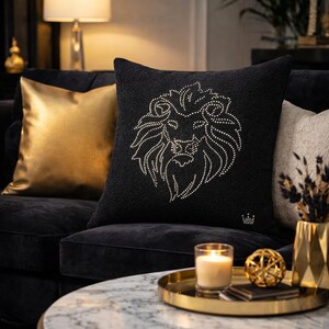 May include: A black decorative pillow with a lion's head design made of small, sparkling embellishments. The pillow is on a black couch with a gold pillow and a gold tray with a candle and decorative sphere.
