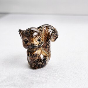 May include: A ceramic squirrel figurine in shades of brown and black. The squirrel is depicted in a sitting position with a bushy tail. The figurine has a glossy finish and detailed features, suitable for home decor.