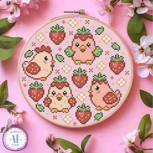 Può includere: Un telaio da ricamo a punto croce con un disegno di fragole e uccelli. Il disegno comprende fragole, uccelli con cappelli di fragole e accenti floreali su sfondo rosa. Il ricamo è in un telaio di legno, con uno sfondo rosa e accenti floreali.