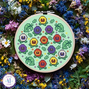 May include: A cross-stitch embroidery hoop featuring a floral pattern with yellow, red, and purple flowers, and green leaf accents on a light green background. The embroidery is set in a wooden hoop and surrounded by a variety of colorful flowers.
