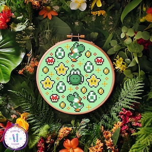 May include: A cross-stitch embroidery hoop featuring a green Yoshi design with stars, eggs, and mushrooms on a light green background. The hoop is set against a backdrop of lush greenery and flowers, creating a vibrant and colorful display.
